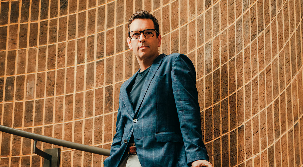 Dressed in a dark blue T-shirt, a blue blazer, and beige slacks, Robert Ford leans casually against the handrail on a curving staircase. Dressed in a dark blue T-shirt, a blue blazer, and beige slacks, Robert Ford leans casually against the handrail on a curving staircase.